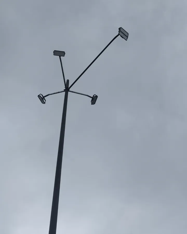 Poste alto con reflectores en sus brazos, visto desde abajo contra un cielo nublado